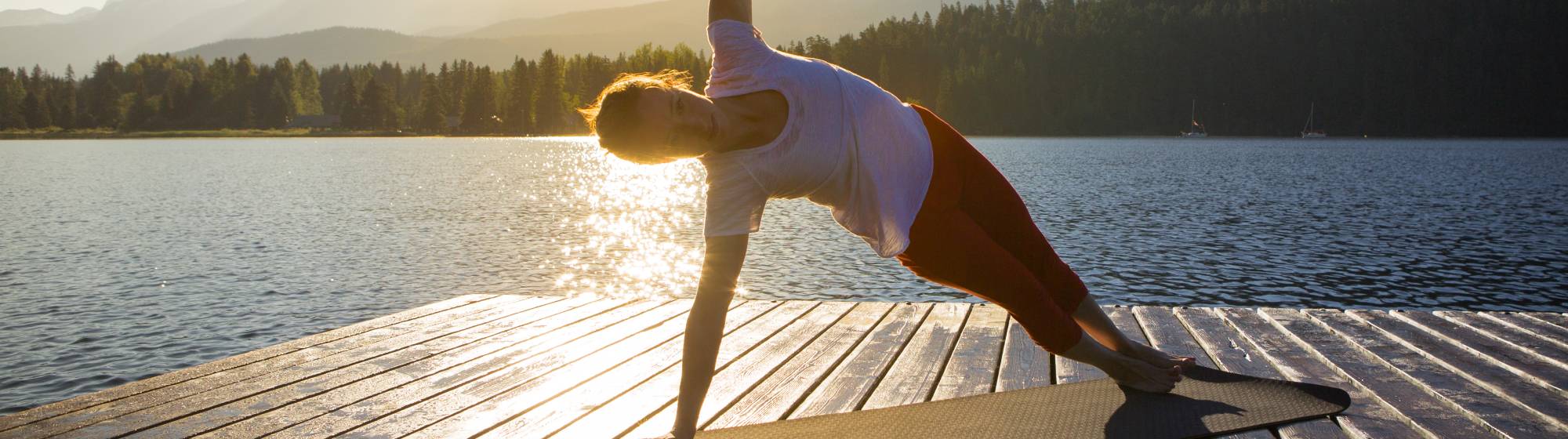 Une dame réalise une pause de yoga face à un lac. 